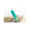 A green tube of lip balm sitting on top of some sand.